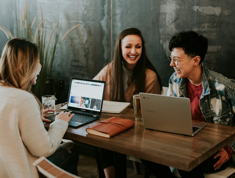 Tres personas riendo alrededor de una mesa con laptops
